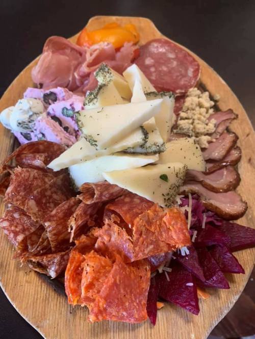 A wooden platter filled with assorted meats, cheeses, and colorful garnishes, showcasing a variety of textures and colors.