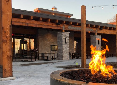 A cozy outdoor space featuring a fire pit, wooden beams, and stone walls, with tables set for dining.