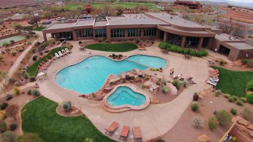 Aerial view of a resort pool area with a large swimming pool, hot tub, and surrounding lounge chairs and greenery.
