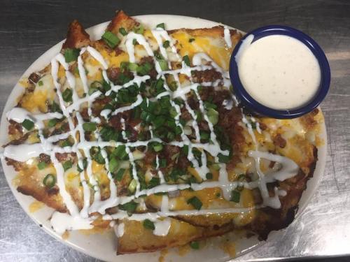 A plate of nachos topped with cheese, green onions, and drizzled with sour cream, served with a side of ranch dressing.