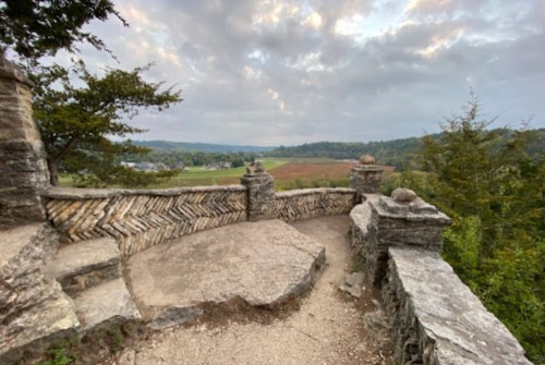 Scenic view from a stone overlook, featuring rolling hills and a cloudy sky in the background.