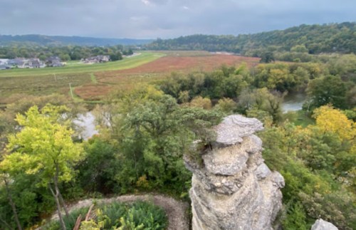 A scenic view from a rocky outcrop overlooking a lush valley with trees and a winding river below.