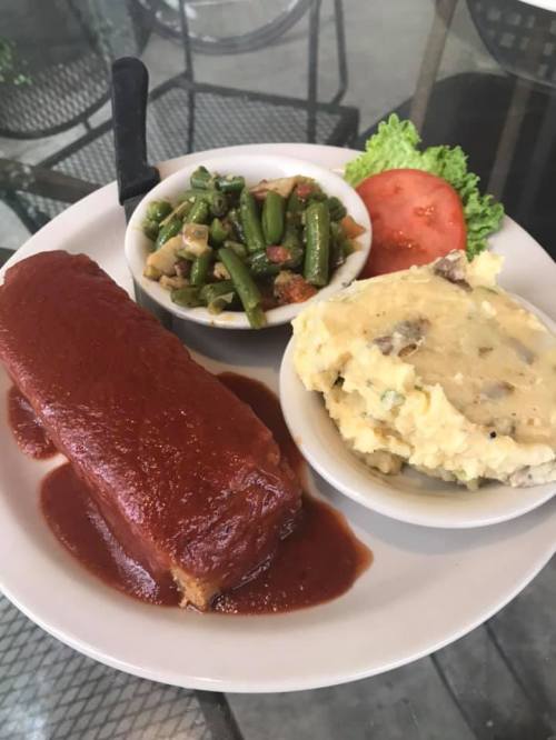 A plate with meatloaf topped with sauce, mashed potatoes, green bean salad, lettuce, and a slice of tomato.