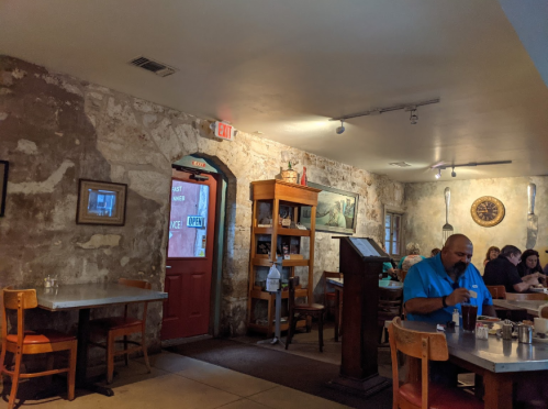 Cozy restaurant interior with stone walls, wooden tables, and patrons dining. A man sits at a table enjoying his meal.