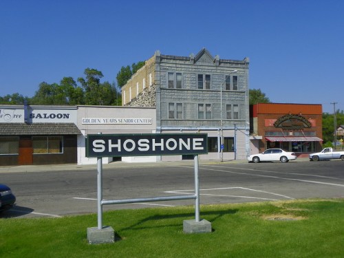 Sign for Shoshone with historic buildings and a clear blue sky in the background.