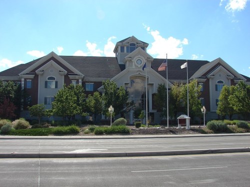 A large, modern building with a clock tower, surrounded by trees and a clear blue sky.
