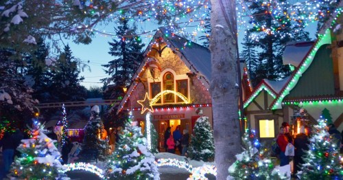 A festive scene with snow-covered trees and colorful lights adorning charming buildings in a winter wonderland.