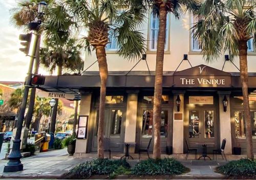 Exterior of The Vendue hotel with palm trees, outdoor seating, and a traffic light in a sunny urban setting.
