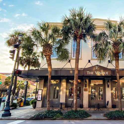 A street view of The Vendue hotel, featuring palm trees and a charming facade in a vibrant urban setting.