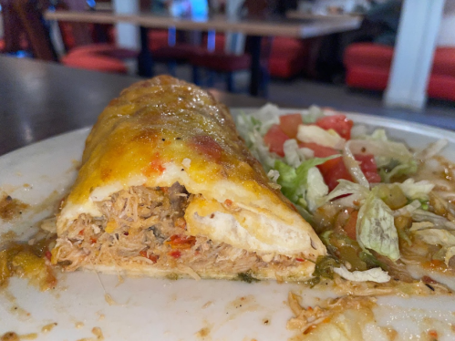 A close-up of a cheesy burrito filled with shredded chicken, served with a side of lettuce and tomato salad.