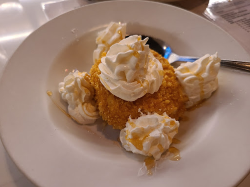 A dessert on a plate featuring a golden, crumbly cake topped with whipped cream and drizzled with syrup.