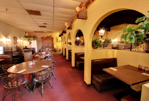 Cozy restaurant interior with arched doorways, wooden tables, and booths, adorned with plants and warm lighting.