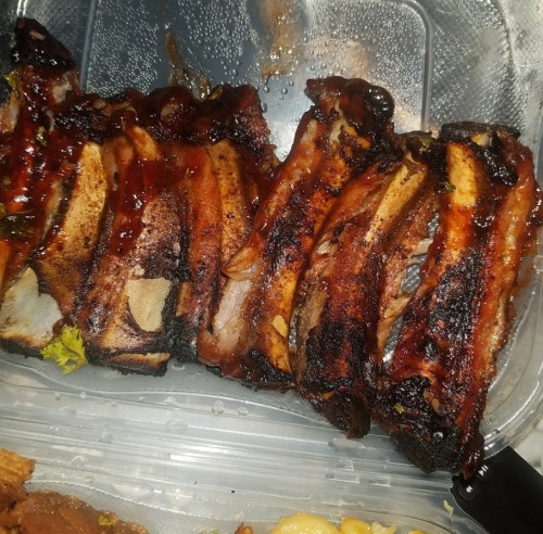 A close-up of grilled ribs coated in barbecue sauce, showing a charred and caramelized exterior.