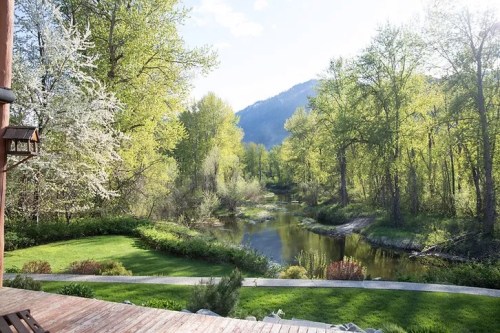 A serene landscape featuring a river surrounded by lush green trees and mountains under a clear blue sky.
