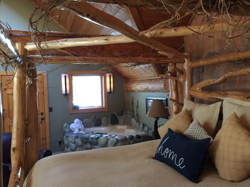 Cozy bedroom with a log frame bed, soft pillows, and a stone accent wall, featuring warm lighting and rustic decor.