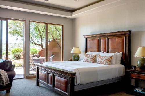 A cozy bedroom featuring a large bed, wooden furniture, and large windows with a view of the outdoors.
