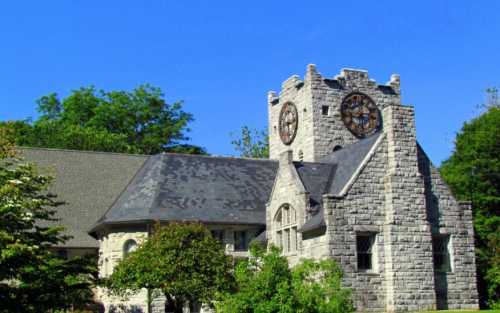 A stone building with a clock tower, surrounded by trees and a clear blue sky.