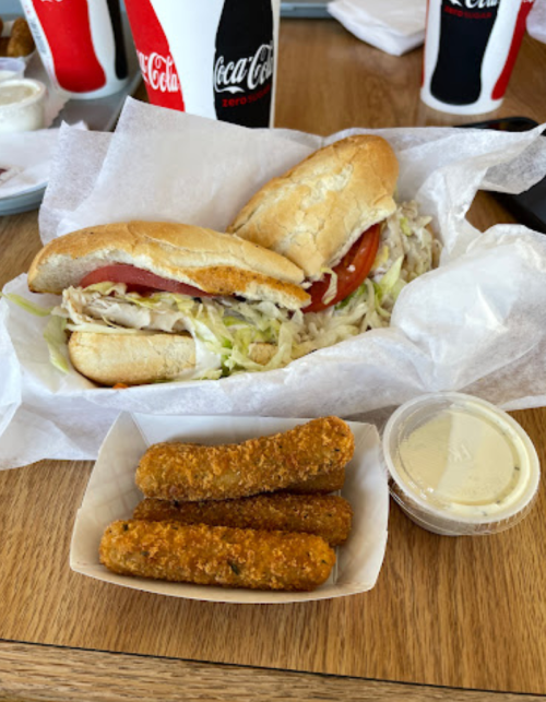 Two sandwiches with lettuce and tomato, accompanied by a side of breaded mozzarella sticks and dipping sauce.