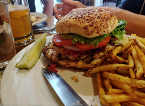 A grilled chicken sandwich with lettuce, tomato, and pickles, served with fries and a pickle on the side.