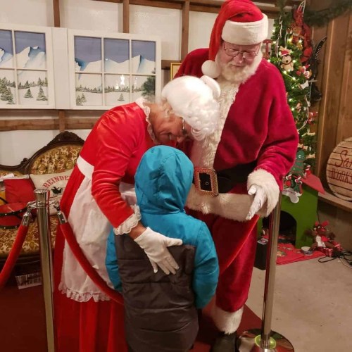 Santa and Mrs. Claus warmly greet a child in a festive setting with holiday decorations.
