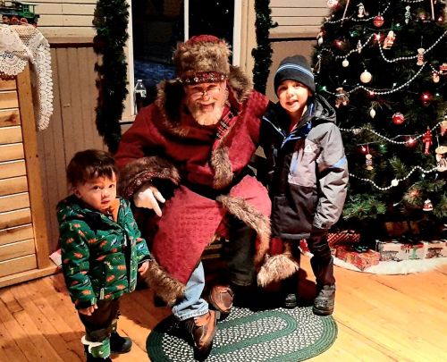 Two children pose with a man dressed as Santa Claus in a festive setting with a decorated Christmas tree.