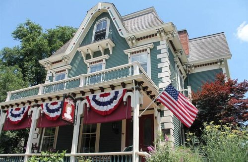 A large, historic green Victorian house adorned with red, white, and blue bunting and an American flag.