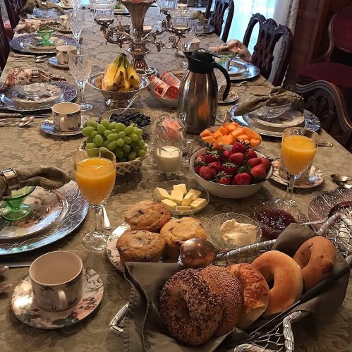 A beautifully set dining table with various fruits, pastries, drinks, and elegant tableware.