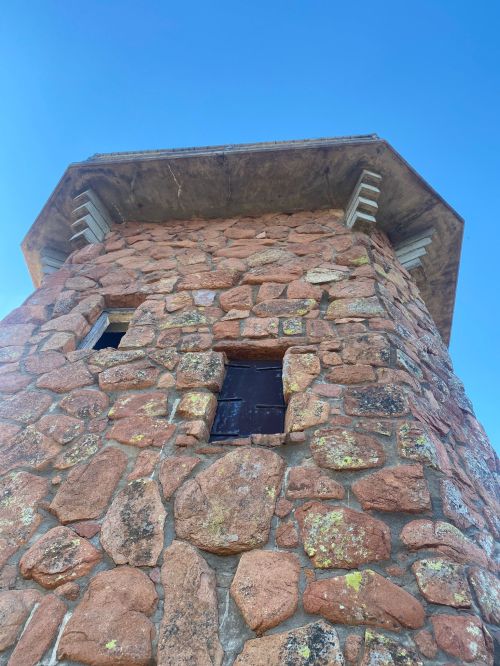 A stone tower with a textured surface and two small windows, set against a clear blue sky.