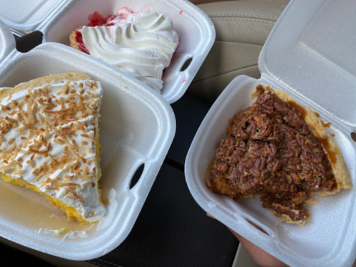 Two takeout containers with slices of coconut cream pie and pecan pie, resting on a car seat.