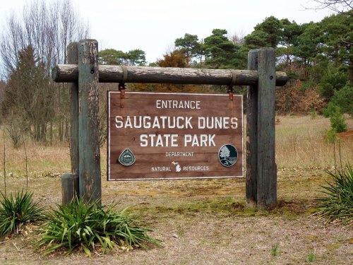 Wooden sign at the entrance of Saugatuck Dunes State Park, featuring park name and natural resources department.