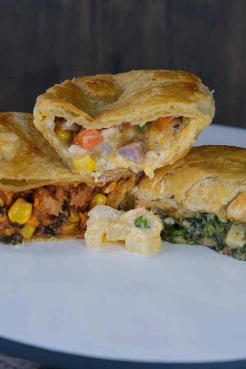 Three savory pastries filled with colorful vegetables, displayed on a white plate against a dark background.