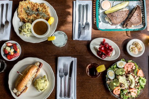 A table set with various dishes: a salad, a sandwich, soup, mashed potatoes, fruit, and dessert, all beautifully arranged.