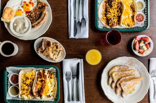 A table set with various breakfast dishes, including tacos, French toast, fruit, and drinks.