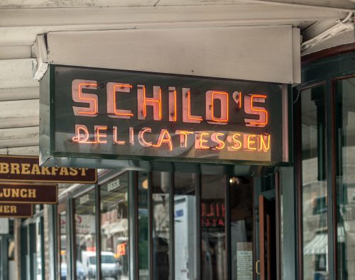 Neon sign for Schilo's Delicatessen, hanging outside a storefront with a vintage aesthetic.