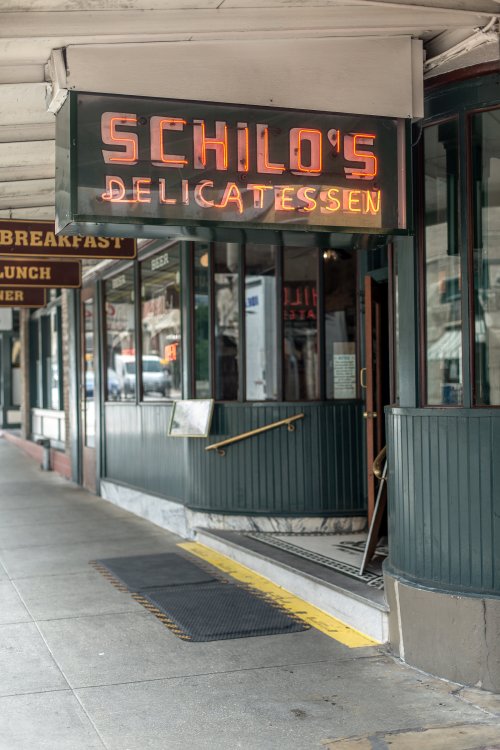 Neon sign for Schilo's Delicatessen outside a storefront, with a sidewalk and entrance visible.