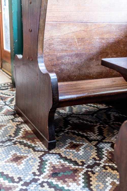 A wooden bench with a curved backrest beside a patterned tile floor.