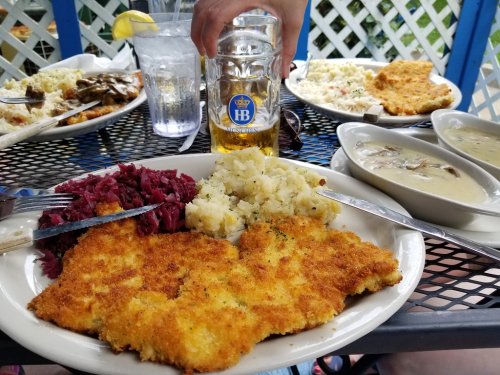 A plate of fried fish with red cabbage, mashed potatoes, and a beer, set on a table with additional dishes in the background.