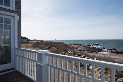 View from a balcony overlooking a rocky shoreline and calm sea under a clear sky.