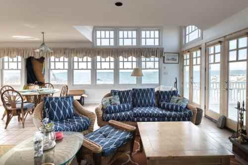 Cozy living room with blue patterned sofas, a wooden table, and large windows overlooking a scenic view.
