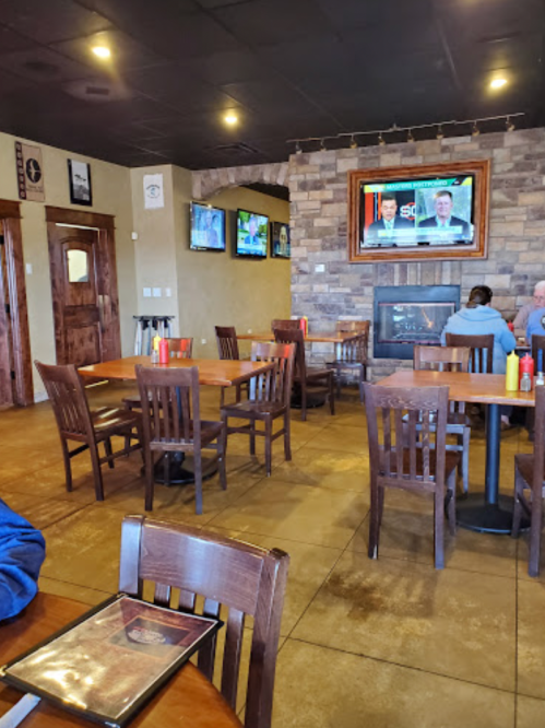Interior of a casual restaurant with wooden tables, chairs, and a TV displaying news on a stone wall.