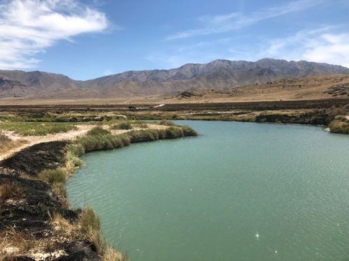 A serene landscape featuring a turquoise river winding through grassy banks, with mountains in the background under a blue sky.