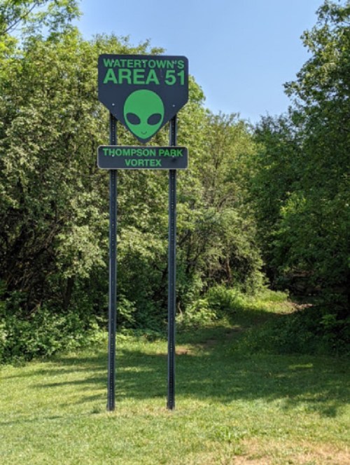 Sign for "Watertown's Area 51" at Thompson Park Vortex, featuring an alien graphic, surrounded by greenery.