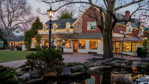 A charming building with warm lights, surrounded by greenery and a pond, at dusk.