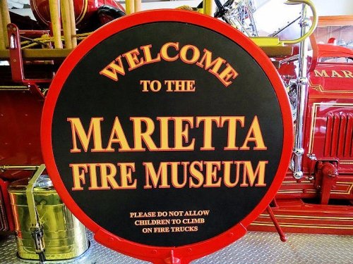 Sign at the Marietta Fire Museum welcoming visitors and advising against climbing on fire trucks.
