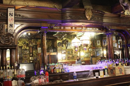 A vintage bar with ornate wooden decor, mirrors, and a variety of colorful bottles on the shelves.