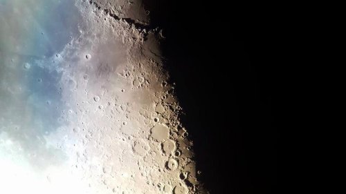 Close-up view of the Moon's surface, showcasing craters and rugged terrain against a dark background.