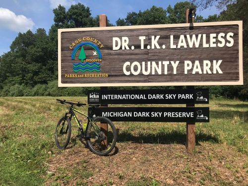 Sign for Dr. T.K. Lawless County Park with a bike parked nearby, surrounded by greenery and trees.