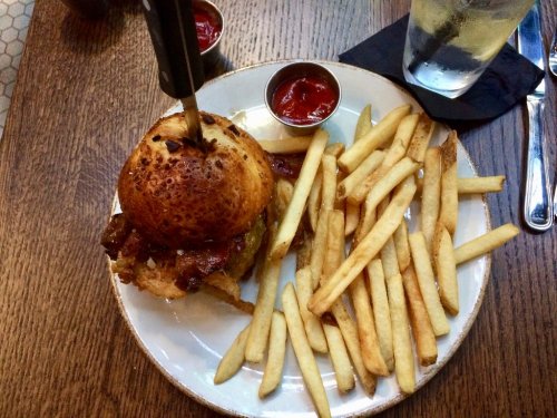 A juicy burger with toppings on a plate, accompanied by a side of golden fries and two small cups of ketchup.