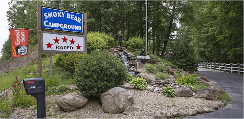 Sign for Smoky Bear Campground featuring a waterfall, greenery, and a rating of five stars.