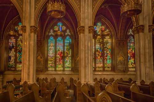 Interior of a church featuring ornate stained glass windows and wooden pews, illuminated by colorful light.